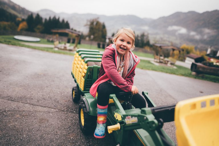 Laughing child on toy tractor in front of Alpine landscape at farm in Salzburger Land